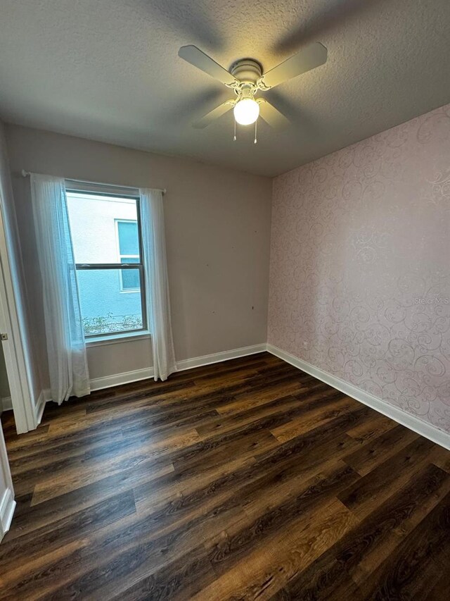 empty room featuring ceiling fan, dark wood-type flooring, and a textured ceiling