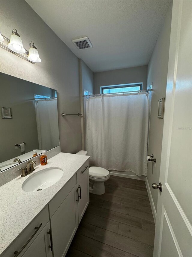 bathroom featuring wood-type flooring, vanity, a textured ceiling, and toilet