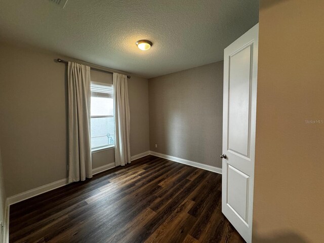 empty room with dark hardwood / wood-style flooring and a textured ceiling