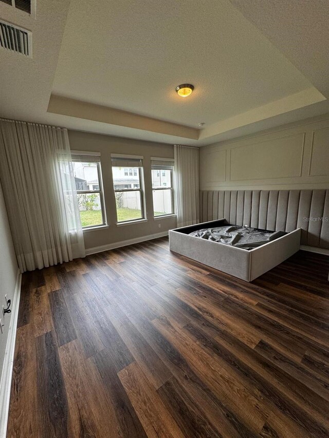 unfurnished bedroom with a raised ceiling, dark hardwood / wood-style floors, and a textured ceiling