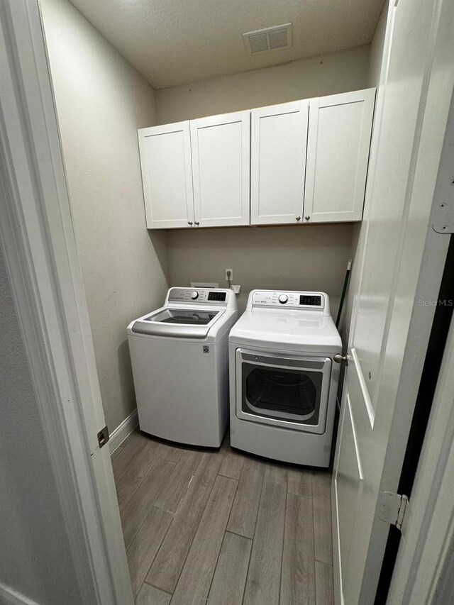 clothes washing area with light hardwood / wood-style floors, cabinets, and washing machine and clothes dryer