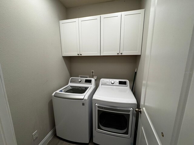 clothes washing area with cabinets and washing machine and dryer