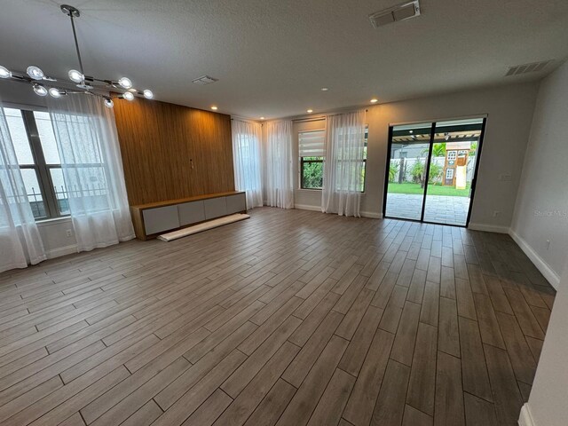 interior space with wooden walls, an inviting chandelier, a textured ceiling, and light wood-type flooring