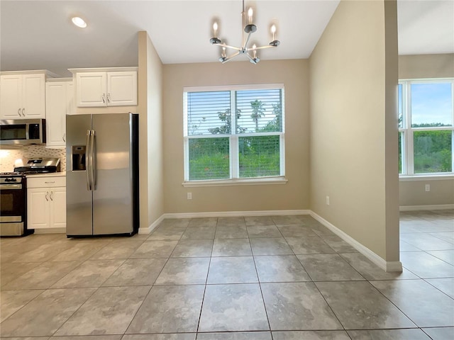 kitchen featuring appliances with stainless steel finishes, light tile patterned floors, a healthy amount of sunlight, white cabinetry, and an inviting chandelier