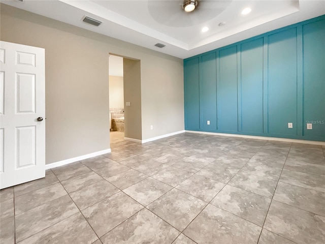 empty room with light tile patterned flooring, ceiling fan, and a tray ceiling