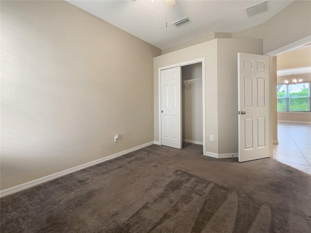 unfurnished bedroom with a closet, ceiling fan with notable chandelier, and dark carpet