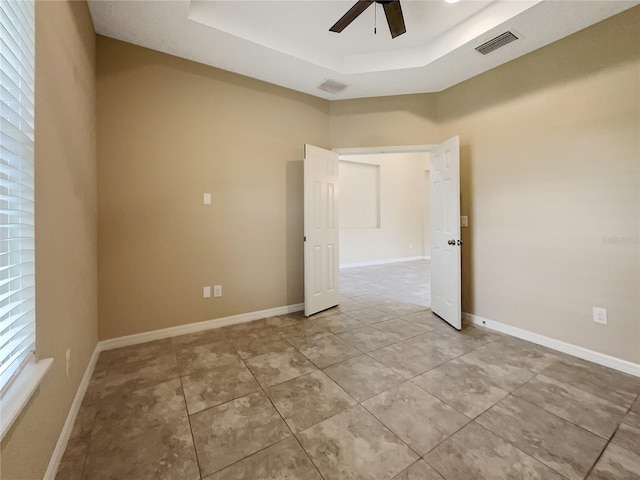 unfurnished room featuring a raised ceiling, ceiling fan, and light tile patterned floors