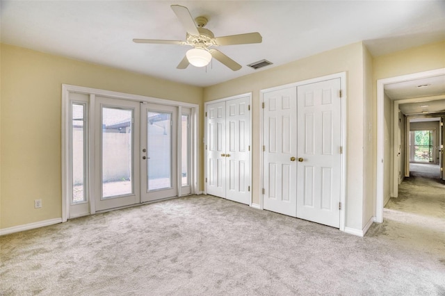 unfurnished bedroom featuring french doors, light colored carpet, access to outside, two closets, and ceiling fan