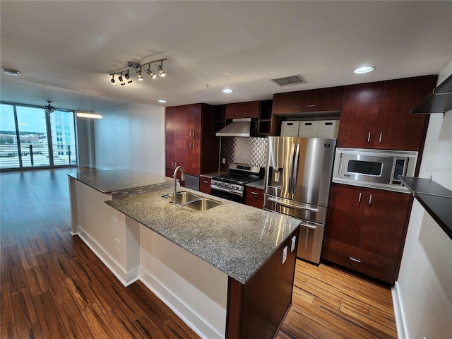 kitchen featuring decorative backsplash, dark stone counters, stainless steel appliances, sink, and a center island with sink