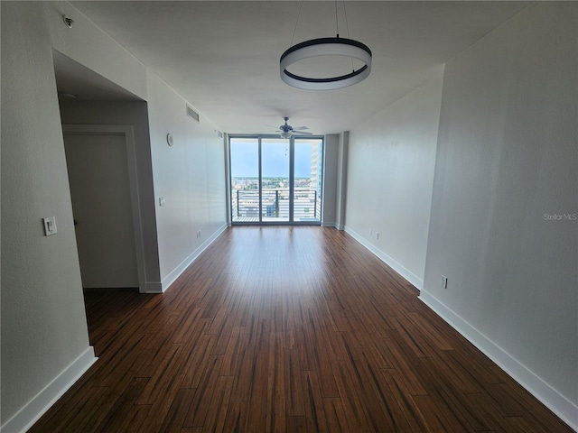 empty room with baseboards, dark wood-type flooring, visible vents, and floor to ceiling windows