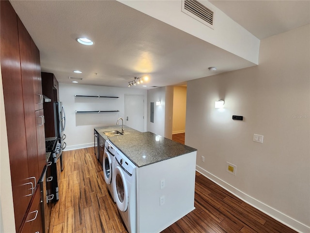 kitchen with dark stone countertops, a kitchen island with sink, sink, and dark wood-type flooring