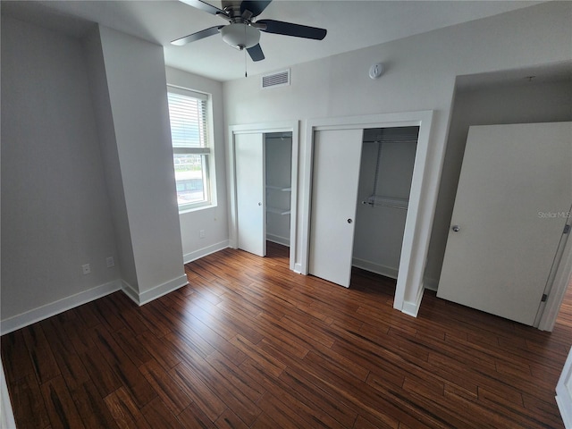 unfurnished bedroom featuring two closets, ceiling fan, and dark wood-type flooring