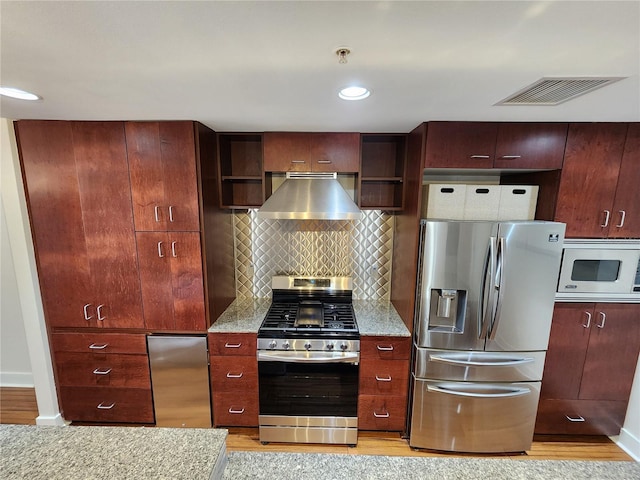 kitchen featuring backsplash, stainless steel appliances, light stone counters, and wall chimney exhaust hood