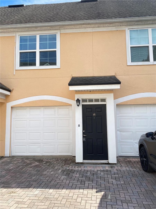 property entrance with stucco siding, an attached garage, and roof with shingles