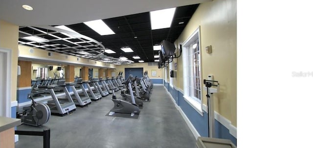 gym with a drop ceiling, a healthy amount of sunlight, and baseboards