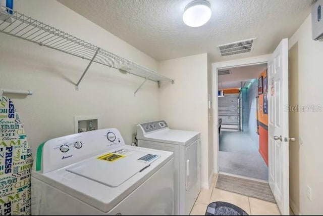 washroom with light tile patterned flooring, washer and dryer, and a textured ceiling