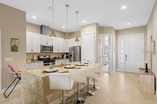 kitchen with white cabinetry, a kitchen island with sink, stainless steel appliances, decorative backsplash, and decorative light fixtures