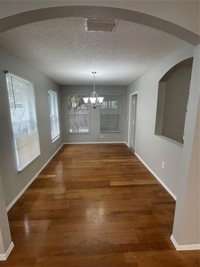 unfurnished dining area featuring an inviting chandelier, a textured ceiling, and dark hardwood / wood-style floors