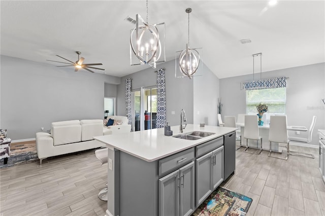 kitchen with light hardwood / wood-style flooring, ceiling fan with notable chandelier, a kitchen island with sink, stainless steel dishwasher, and sink