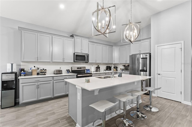 kitchen featuring hanging light fixtures, light wood-type flooring, sink, a center island with sink, and appliances with stainless steel finishes