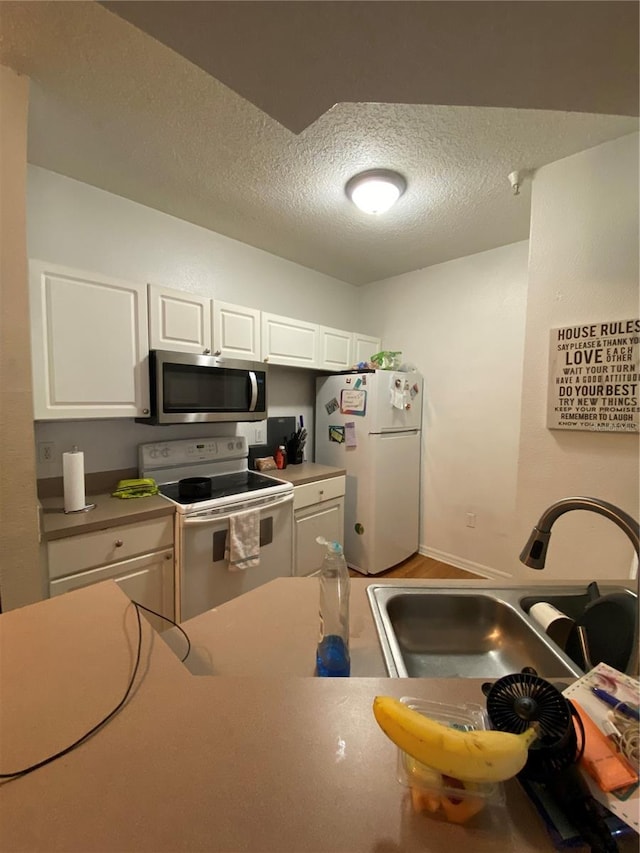 kitchen with sink, a textured ceiling, white cabinetry, and white appliances