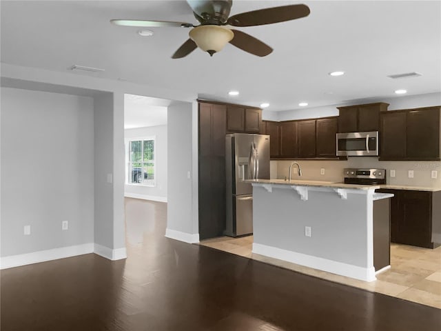 kitchen featuring a kitchen breakfast bar, sink, ceiling fan, an island with sink, and appliances with stainless steel finishes