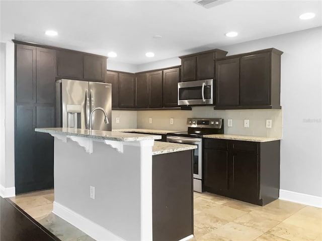 kitchen with sink, light stone countertops, an island with sink, dark brown cabinetry, and stainless steel appliances