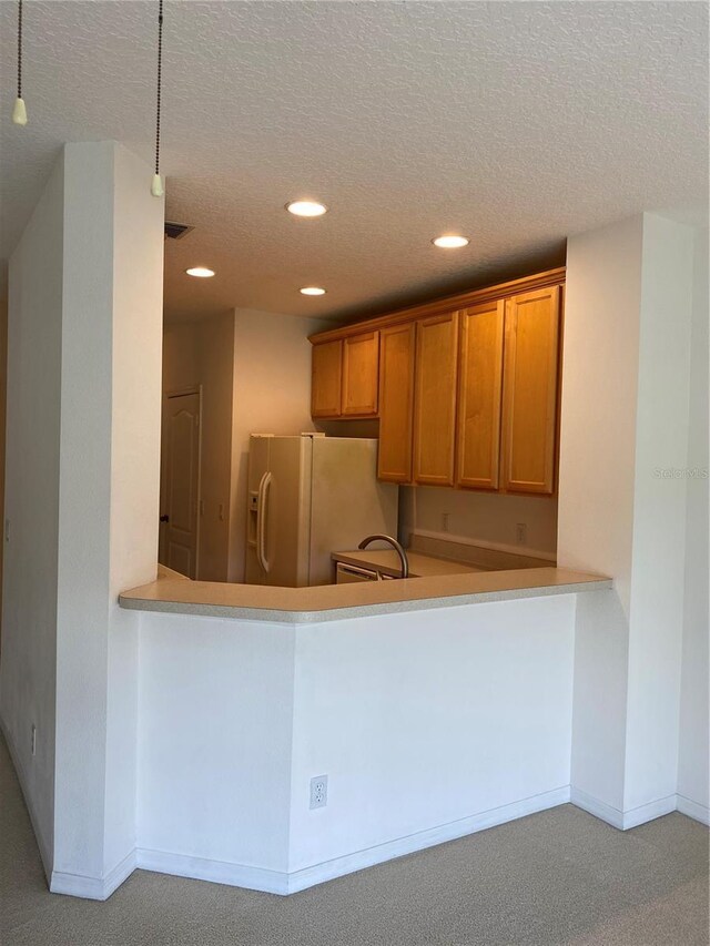 kitchen featuring sink, white fridge with ice dispenser, light carpet, and a textured ceiling