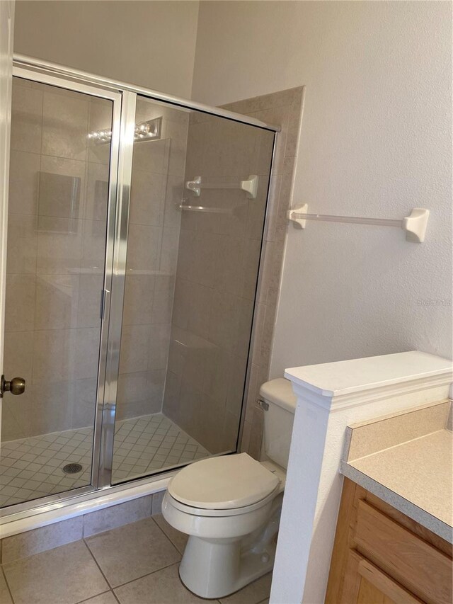 bathroom with tile patterned flooring, walk in shower, vanity, and toilet