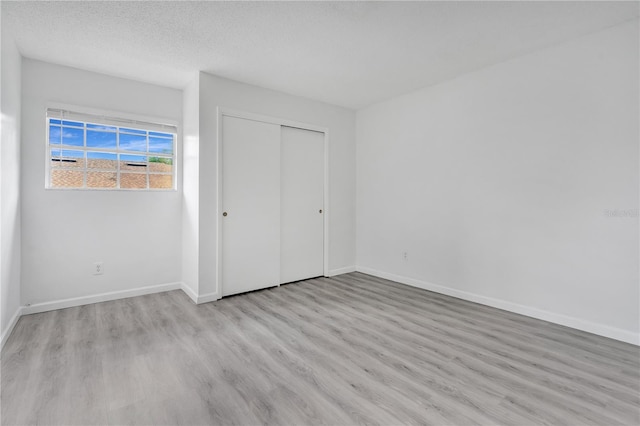 unfurnished bedroom with a textured ceiling, light hardwood / wood-style floors, and a closet