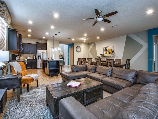 living room with a textured ceiling, ceiling fan, and light tile patterned floors