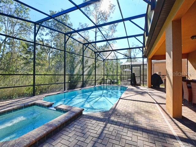 view of swimming pool with an in ground hot tub, a patio area, and glass enclosure