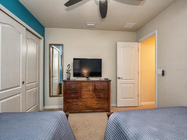 bedroom with a closet, a textured ceiling, ceiling fan, and light colored carpet