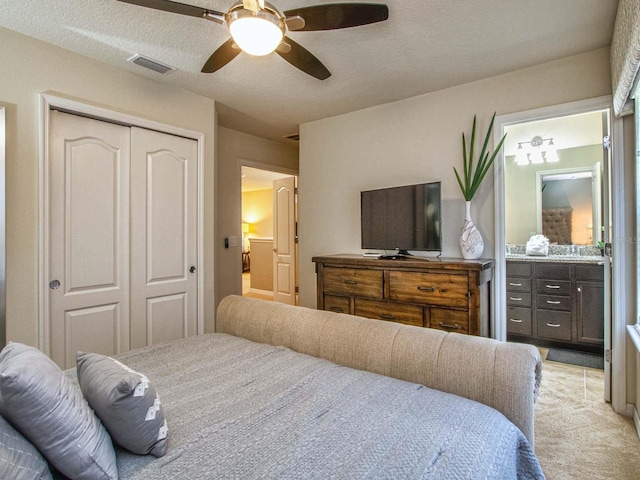 bedroom with a textured ceiling, ceiling fan, ensuite bathroom, light carpet, and a closet