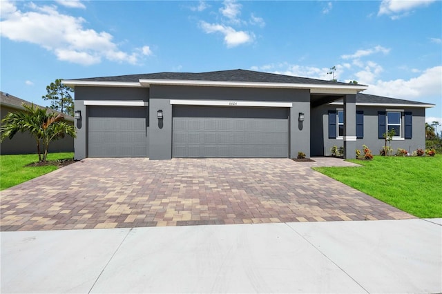 view of front of house with an attached garage, decorative driveway, a front yard, and stucco siding