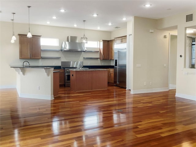 kitchen with dark hardwood / wood-style flooring, pendant lighting, stainless steel appliances, and wall chimney range hood