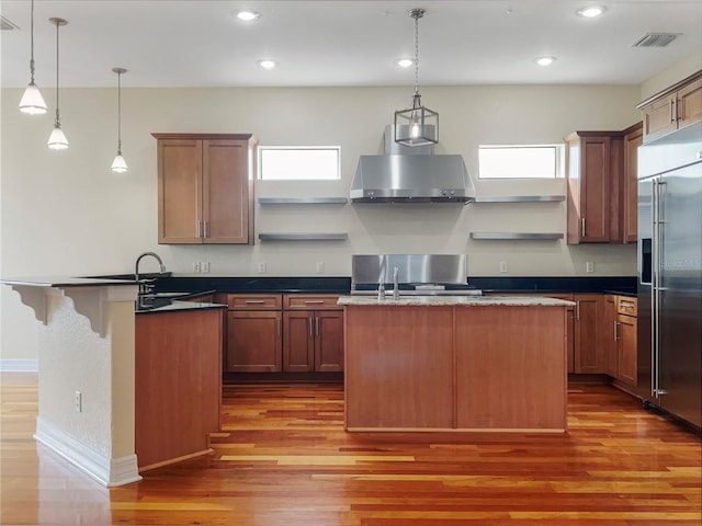 kitchen featuring a wealth of natural light, decorative light fixtures, high end fridge, and range hood