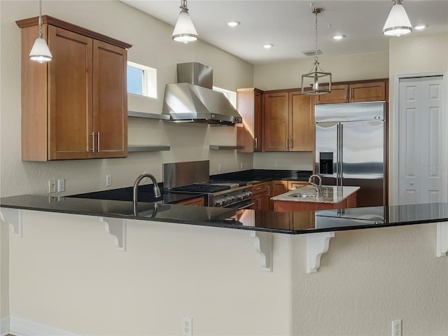 kitchen with a breakfast bar area, pendant lighting, wall chimney range hood, and appliances with stainless steel finishes