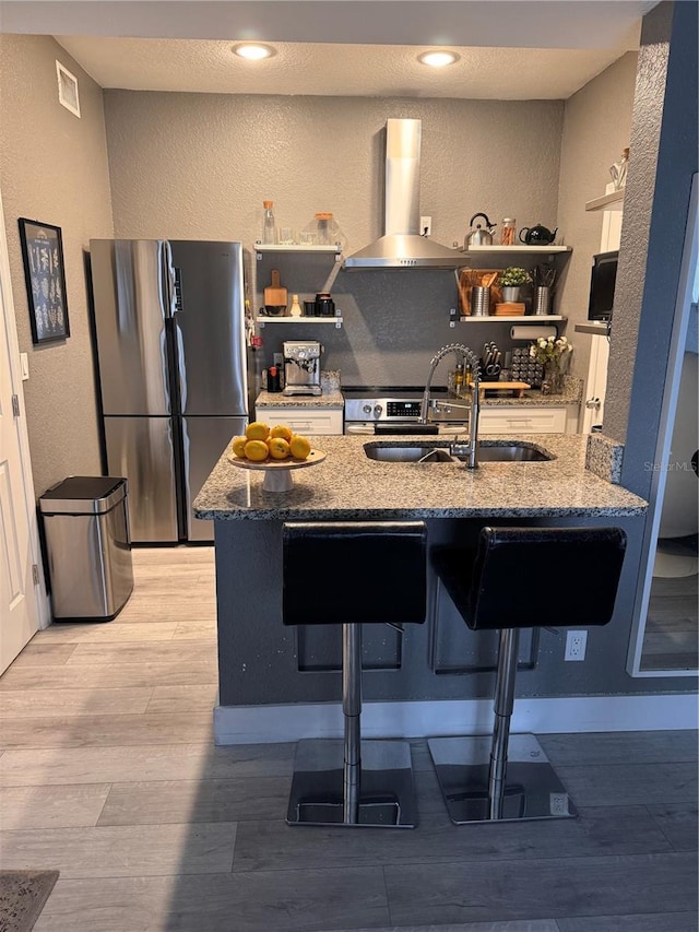 kitchen featuring sink, stainless steel fridge, a breakfast bar area, ventilation hood, and stone countertops