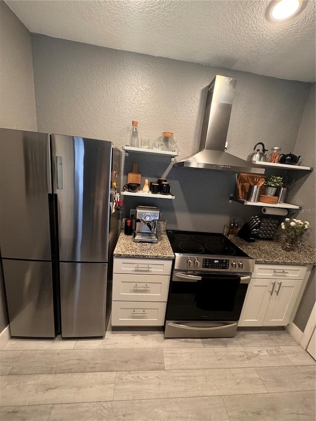 kitchen with a textured ceiling, wall chimney range hood, stone counters, stainless steel appliances, and white cabinets