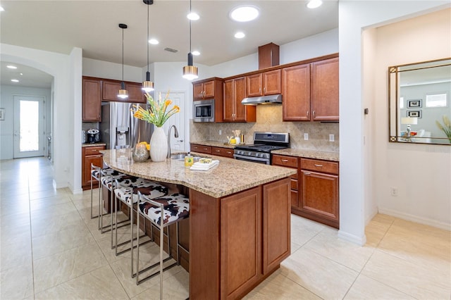 kitchen featuring decorative backsplash, light stone counters, stainless steel appliances, a kitchen island with sink, and decorative light fixtures