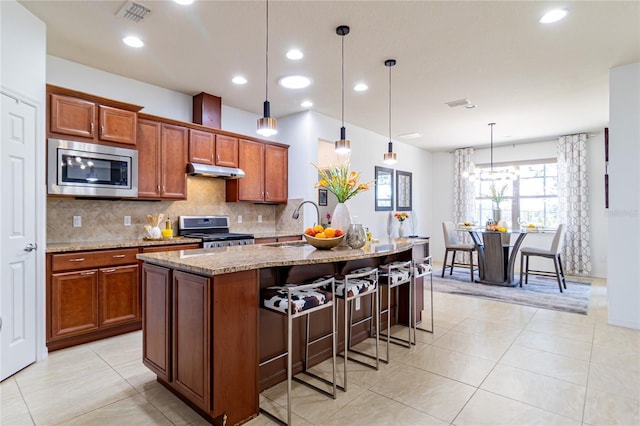 kitchen with a breakfast bar, stainless steel appliances, sink, hanging light fixtures, and an island with sink