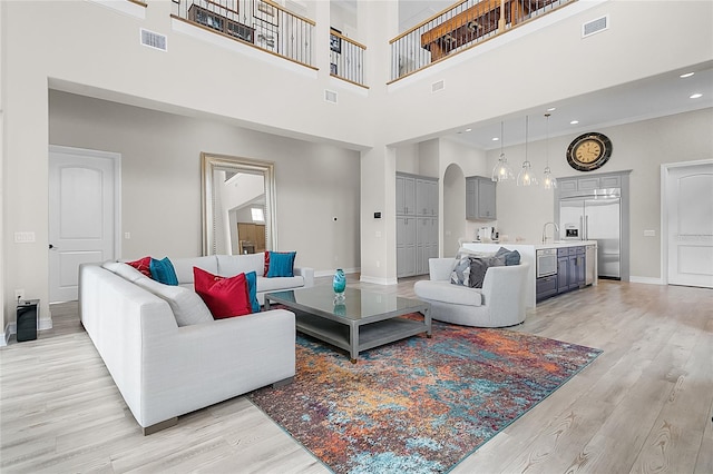 living room with a towering ceiling, sink, and light hardwood / wood-style flooring