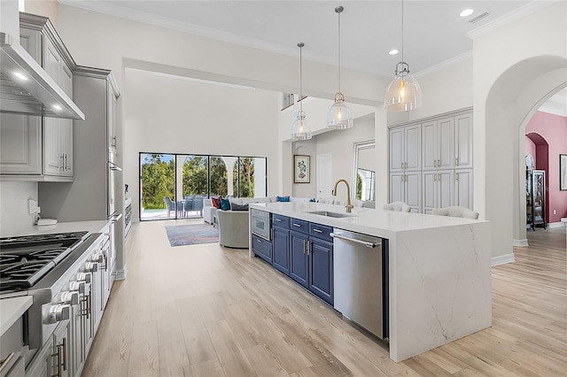 kitchen featuring wall chimney exhaust hood, light hardwood / wood-style floors, hanging light fixtures, stainless steel appliances, and sink