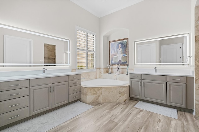 bathroom featuring vanity, a relaxing tiled tub, and wood-type flooring