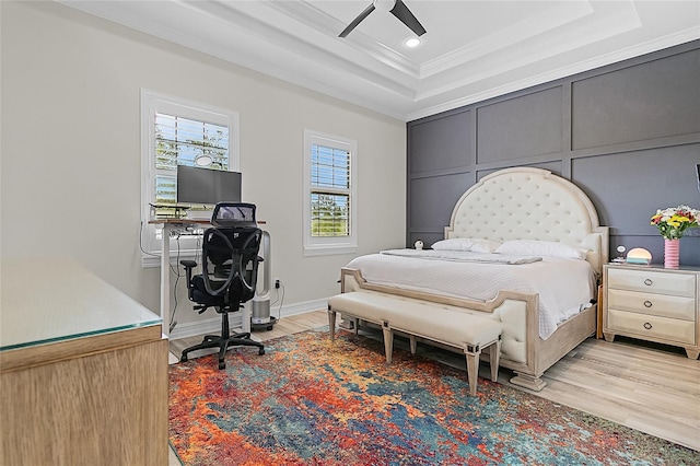 bedroom featuring light hardwood / wood-style flooring, a tray ceiling, ornamental molding, and ceiling fan