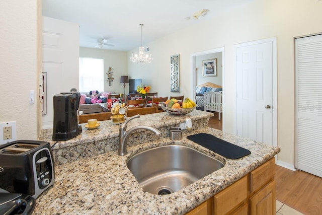 kitchen featuring sink, light stone counters, pendant lighting, ceiling fan with notable chandelier, and light wood-type flooring