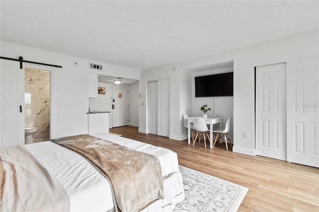 bedroom featuring multiple closets, a barn door, connected bathroom, and light wood-type flooring