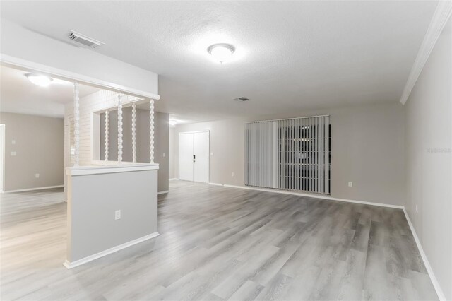 spare room featuring crown molding, a textured ceiling, and light hardwood / wood-style flooring