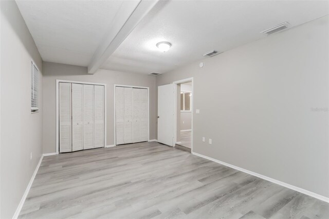 unfurnished bedroom with multiple closets, light hardwood / wood-style floors, and beam ceiling